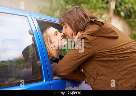 Lingering goodbyes. a young couple kissing each other goodbye through a ...