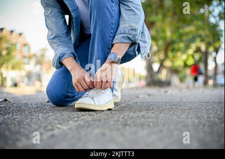 Asian male traveler in casual clothes tying his shoes laces on the street. cropped image Stock Photo