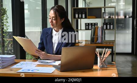 Professional millennial Asian businesswoman or female manager is reading a document, checking her financial report, and working at her desk in the off Stock Photo