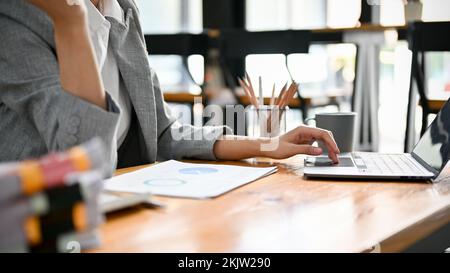 cropped image, Professional Asian businesswoman using her laptop computer, typing on keyboard, searching online information, managing her task on comp Stock Photo
