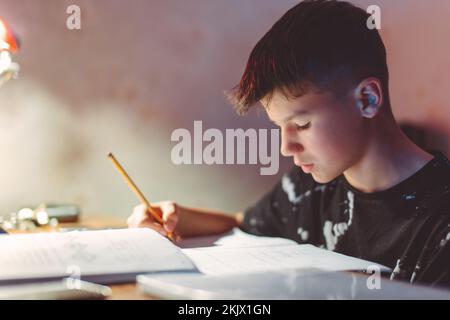 Young diligent Caucasian boy thinking while doing homework at evening Stock Photo