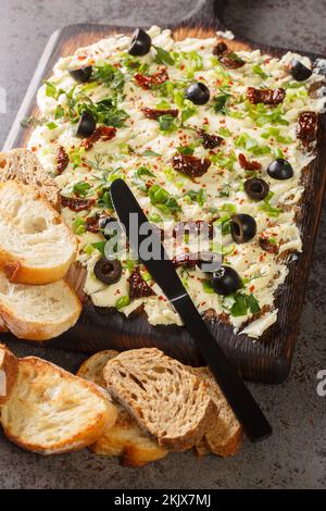 Homemade Trendy Butter Board with Herbs, olives, sun-dried tomatoes and Bread closeup on the table. Vertical Stock Photo
