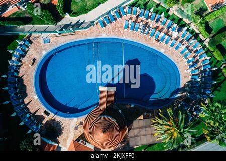Top down aerial view of hotel swimming pool with crystal blue water surrounded with palm trees and deck laying chairs in resort Stock Photo