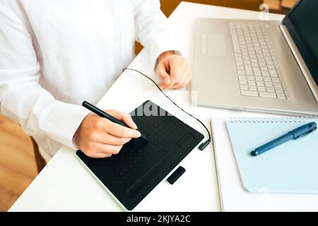 Young woman graphic designer hands - using laptop computer and graphic tablet in the modern interior. Freelancer digital artist working remotely from Stock Photo