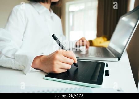 Faceless image of young woman graphic designer or digital artist using laptop computer and graphic tablet in the modern interior. Freelancer working r Stock Photo