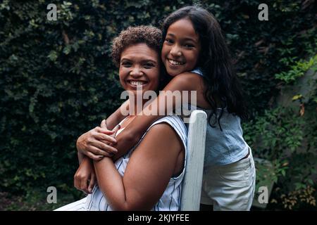 Smiling girl and her grandma looking at the camera. Grandmother and granddaughter hugging outdoors. Stock Photo