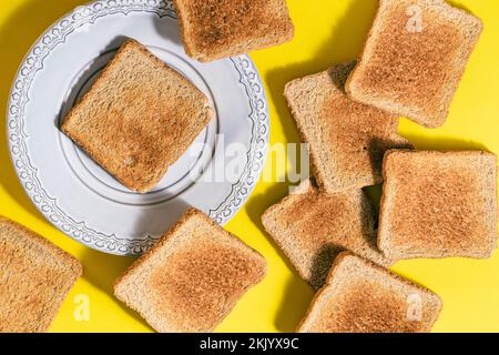 Gray plate with slice of toasted bread and several slices of toasted bread scattered on yellow background Stock Photo