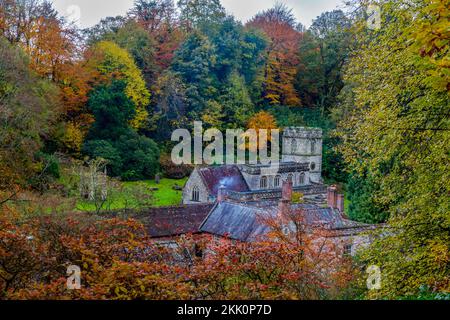 Spectacular autumn colour on the woodland trees, a smoking chimney and the parish church at Stourhead Gardens, Wiltshire, England, UK Stock Photo