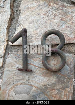 A stone wall with the number 18 on it in rusty iron digits - vertical shot Stock Photo