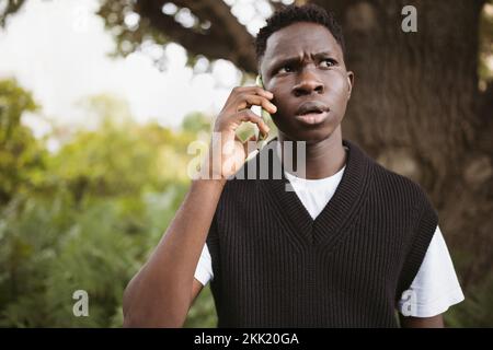 Young African man talking on phone shocked, stressed. Street portrait, copy space Stock Photo