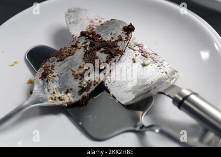 Multiple dirty cake servers on a white plate. These cake serving tools have a lot of cake pieces - uncleaned, not yet washed. Stock Photo