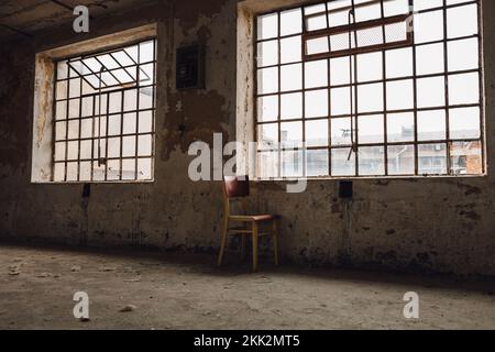 Abandoned old factory room with gridded wide windows on the old vintage wall. Lonely old chair near the window. Grunge image concept image. Stock Photo