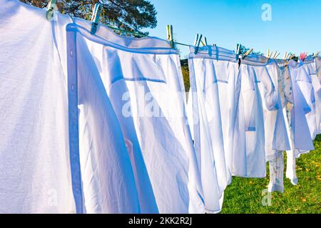 White shirts and clothes drying outside on a washing line with a blue sky on a clear, sunny autumn day. Stock Photo