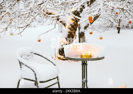Snow covering apple tree in home garden in winter, decorated with lot of copper metallic Christmas baubles and warm white string led lights. Stock Photo