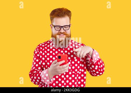 Cheerful bearded chubby man enjoys using mobile application installed in his modern smartphone. Stock Photo