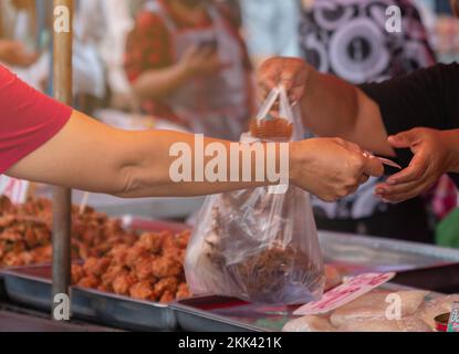 Woman hand hold money to buying fire fish and other food on street food market. Stock Photo