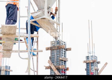 Worker pour concrete from bucket for cast the structural columns in building site. Stock Photo