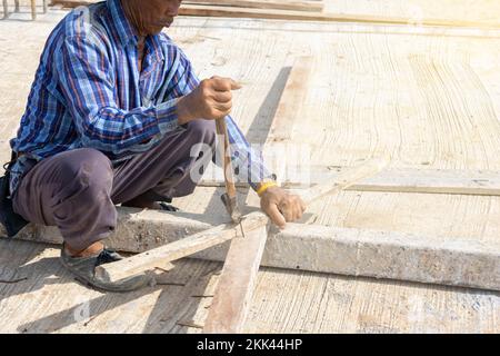 Worker use hammer remove nails on wood stick in construction site. Stock Photo