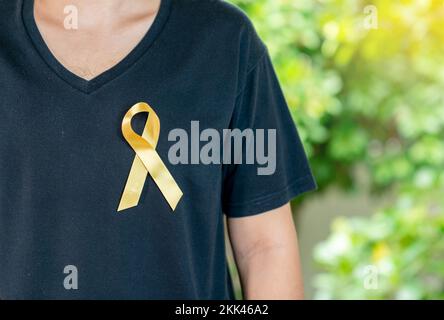 Yellow ribbon on chest, the man in black shirt on out of focusl background, international childhood cancer day concept Stock Photo