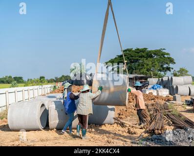 Workers are sorting large concrete pipes at a construction site. Mobile crain lifting Stock Photo