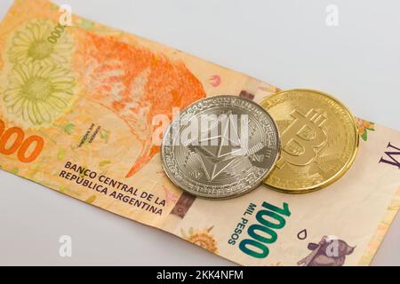 Physical Bitcoin and Ethereum coin over a thousand argentinian pesos  bill on white background. Cryptocurrency exchange, investment concept. Stock Photo
