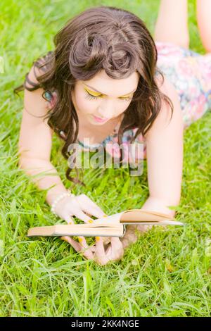 Gorgeous Woman Of Spring Lays Down On A Open Rural Grassland Meadow While Reading Chapters From A Story Book In A Springtime Concept Stock Photo