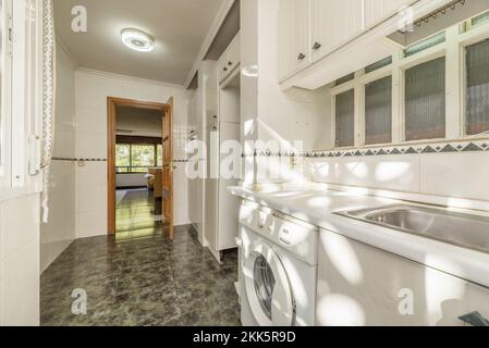 Kitchen with white lacquered wood furniture, stoneware walls, green stoneware floor and white countertop with sunbeams bathing the surface Stock Photo