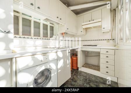 Kitchen with white lacquered wood furniture, stoneware walls, green stoneware floor, butane cylinders for the burners and white countertop with sunbea Stock Photo