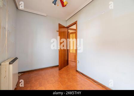 Empty bedroom with dirty walls, orange tiled floor, dark colored wooden simple access door and electric heater Stock Photo