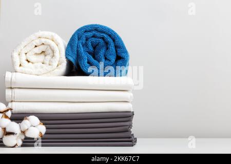 A stack of bed linen, rolls of blue and white towels on the table. Stock Photo
