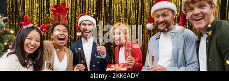 Positive interracial business people with champagne glasses standing under confetti during Christmas party in office, banner Stock Photo