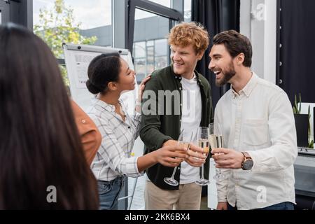 Smiling multiracial businesswoman talking to colleagues with champagne in office Stock Photo