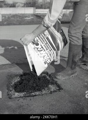 1980s, re-surfacing, a man using a bag of a new construction product to patch or repair a driveway, a ready-mix or ready to lay black tarmacmacadam or asphalt, known as a cold-lay tar, England, UK. Stock Photo