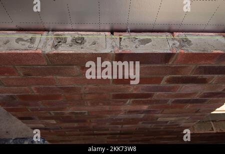 Close-up view of a partially constructed red brick wall with visible mortar and alignment string during building work Stock Photo
