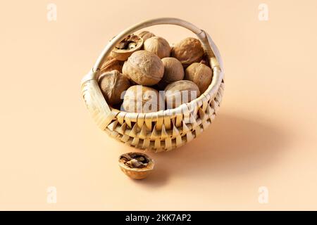 A beige basket with walnuts on an orange background and half a cracked walnut on the table Stock Photo