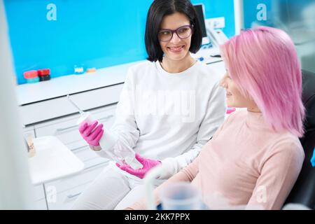 Woman dentist in pink gloves shows an irrigator to patient Stock Photo
