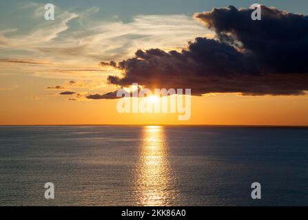 The sunset view of a sun half hidden behind the dark cloud over Gulf of Riga (Latvia). Stock Photo