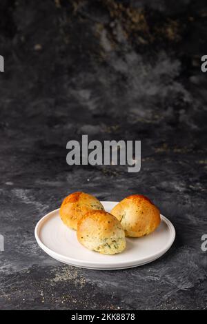 A vertical closeup of a traditional Turkish savory pastry pogaca on a white plate isolated on a dark background. Stock Photo