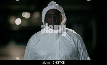 Upset unhappy tired man posing on dark background serious male doctor medical laboratory worker lifeguard in white protective chemical suit uniform Stock Photo
