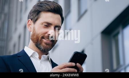 Close-up elegant handsome bearded man holding phone sends email communicates on internet successful businessman planning organizes schedule using Stock Photo