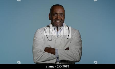 Mature confident happy doctor standing in gray background studio with arms crossed glad smiling african american man professional therapist physician Stock Photo