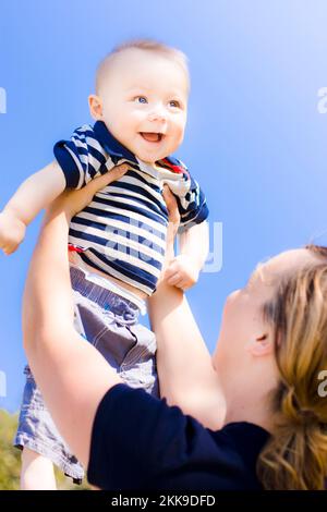 Smiling baby held up to the sky by mother Stock Photo