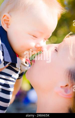 Joyful young baby with a big grin rubbing noses with Mom as he is held aloft prior to being kissed by her Stock Photo