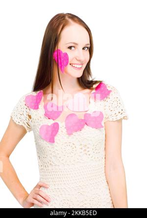 Cute Brunette Girl Smiling While Wearing Pink Paper Shaped Hearts All Over Her Face And Body In A Romantic Love Letters Concept, Isolated On White Bac Stock Photo