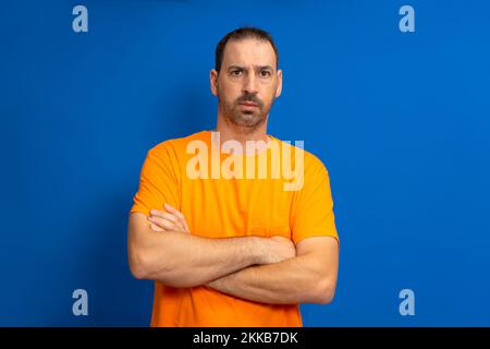 Serious latin man with beard posing with arms crossed isolated on blue studio background. Stock Photo