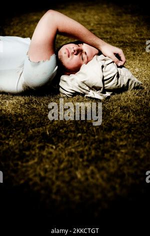 Tired Of Being Broke A Unfortunate Homeless Man Uses On His Sack Of Belongings As A Pillow While Sleeping Outdoors In A Grass Field At Nighttime Stock Photo