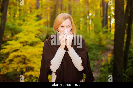 Woman blowing nose with handkerchief In autumn park. Seasonal virus infection. Chronic disease Stock Photo