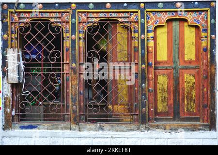 Decorative metal grillwork and vintage painted shutters cover a series of windows framed by traditional painted woodwork in Thimphu, Bhutan. Stock Photo