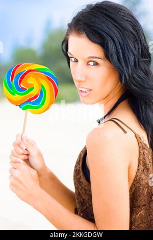 Attractive Female Holding Big Rainbow Candy Lollipop With Intense Expression As If She Has An Insatiable Craving For Candy Stock Photo