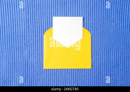 Yellow envelope with blank card on purple knitted fabric background. Birthday, invitation, holiday concept. Top view, flat lay. Stock Photo